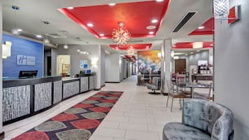 Zona de recepción de hotel con diseño moderno, que incluye un mostrador de recepción, área de descanso y un pasillo que conduce a otras habitaciones.