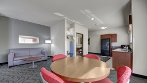 A conference room with a round table and six chairs, a sofa, a kitchenette, and a mirror.