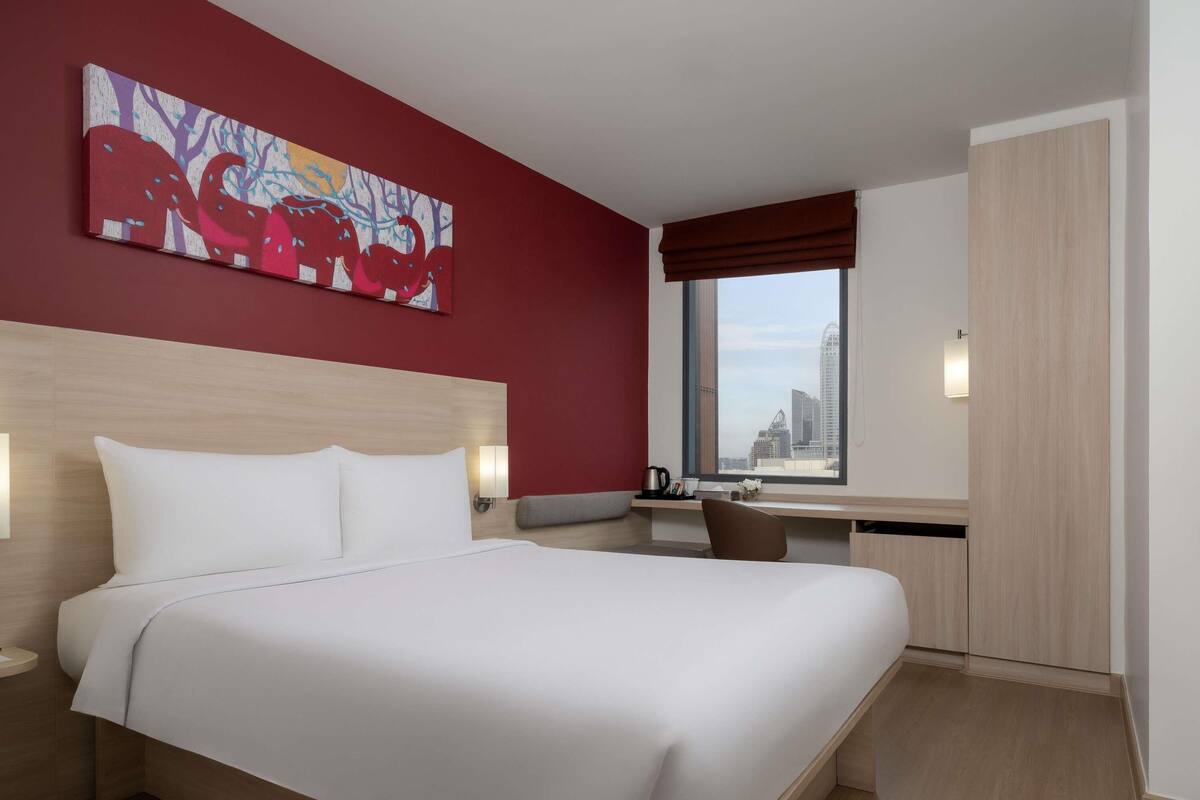 Una habitación de hotel moderna con una cama grande, un escritorio y vistas a la ciudad.