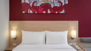 Habitación de hotel con cabecera de madera, ropa de cama blanca, dos lámparas de noche, un teléfono y un cuadro sobre la cama.