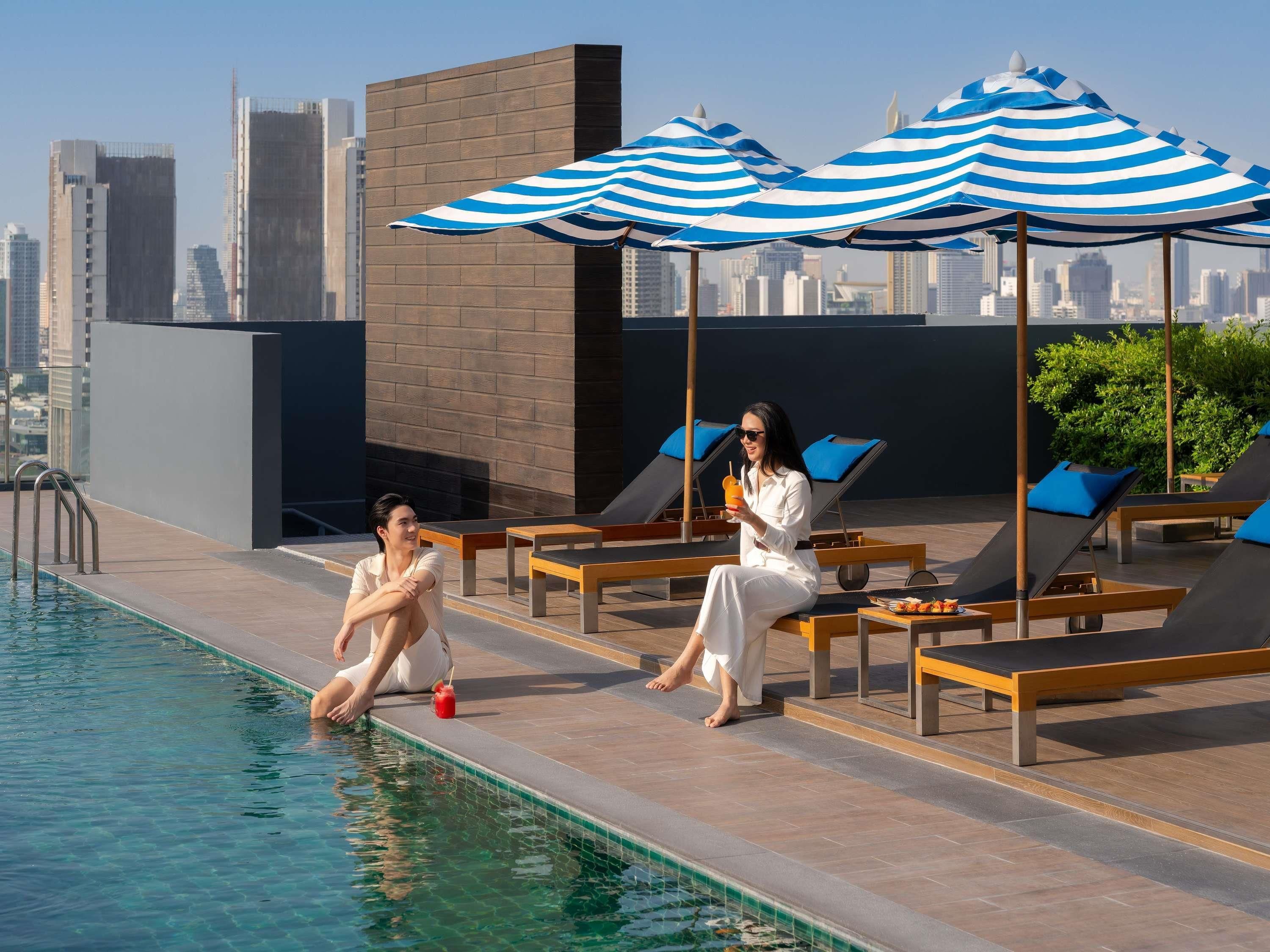 Une piscine sur le toit, agrémentée de chaises longues et de parasols, avec une vue sur les toits de la ville en arrière-plan et un ciel dégagé.