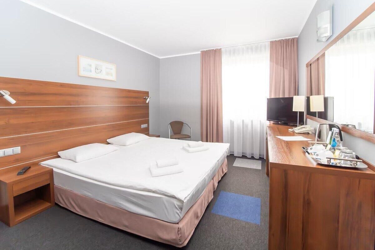 A hotel room with a large bed, bedside tables, a desk with a chair, a TV, and a window with curtains.