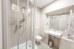 Uma casa de banho moderna com chuveiro em cabine de vidro, sanita e lavatório com espelho em cima.