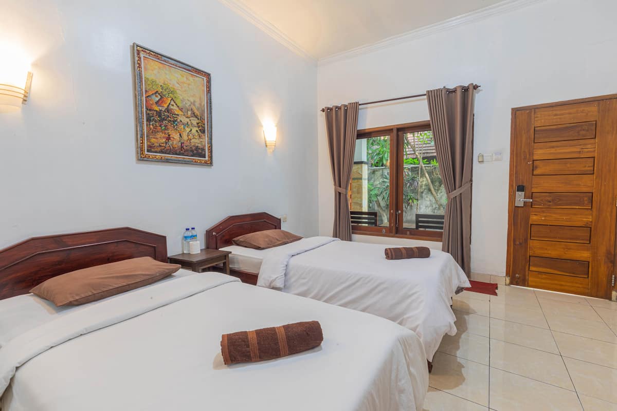 A hotel room with two beds, a wooden door, a window with curtains, a wall-mounted painting, and a nightstand with a bottle.