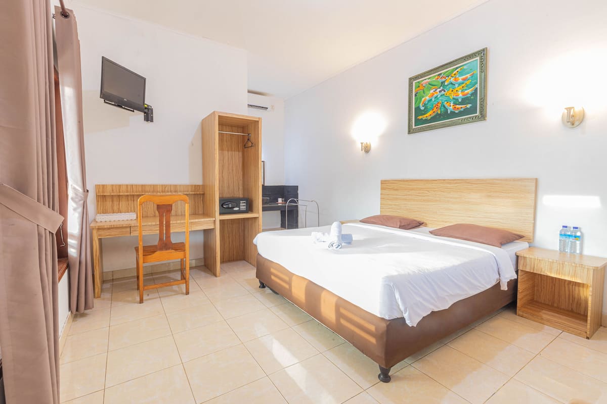 A hotel room with a bed, a desk, a chair, a wardrobe, and a TV on the wall.