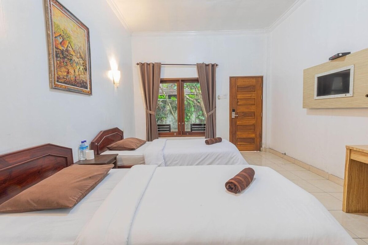 A hotel room with two beds, a wooden headboard, a TV mounted on the wall, and a window with curtains.