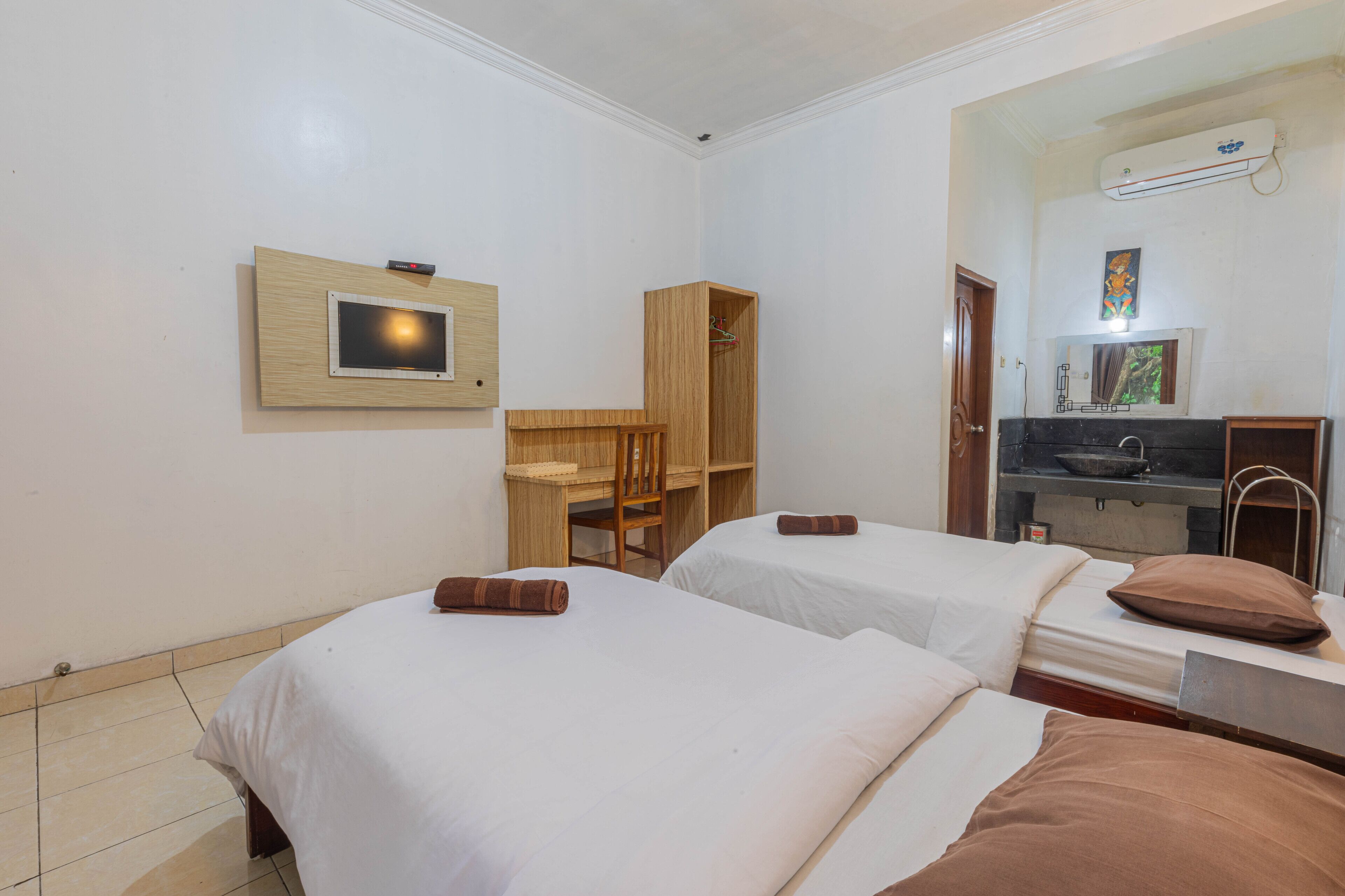 A hotel room with two beds, a wooden desk, a small shelf, and a mirror.