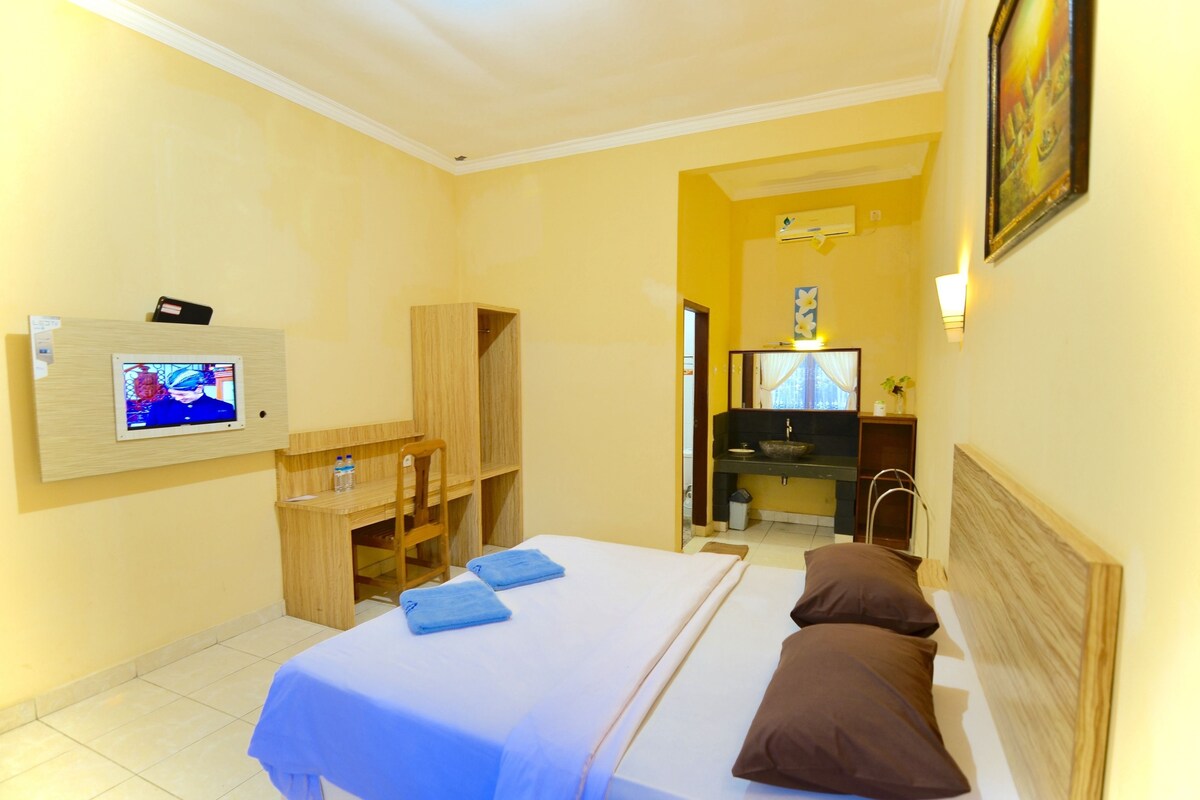 A hotel room with a bed, a desk, a chair, a television, and a bathroom visible through an open door.