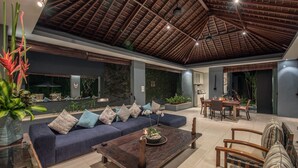 A spacious living area with a dark blue sofa, wooden coffee table, and a dining table set for four. - Kembali Villas (Seminyak)