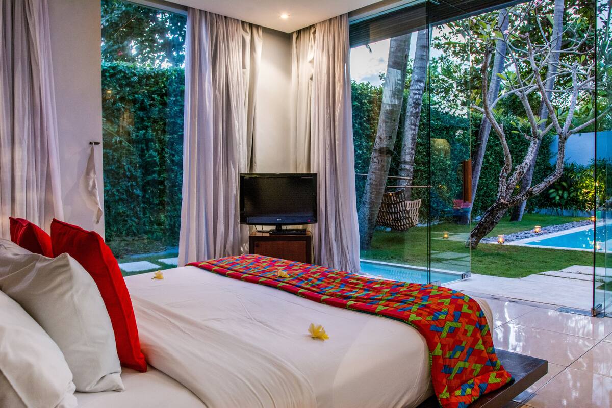 A bedroom with a large bed, a TV, and a view of a swimming pool and garden.