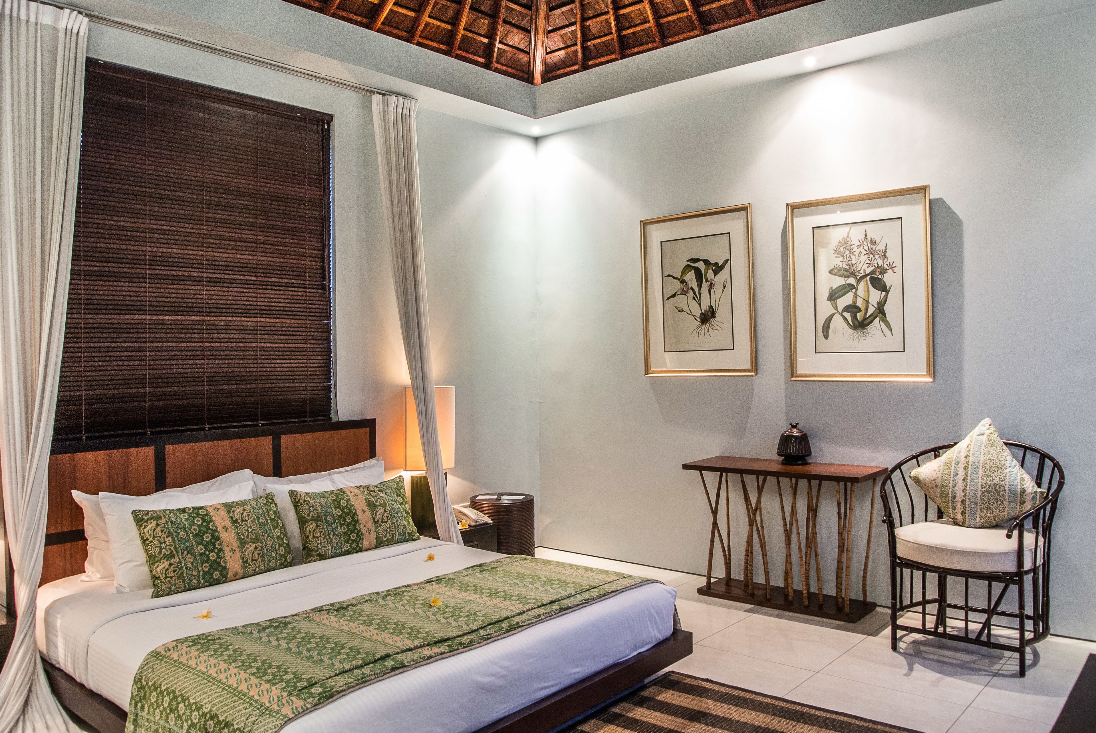 A bedroom with a bed, bedside table, chair, and artwork on the wall.