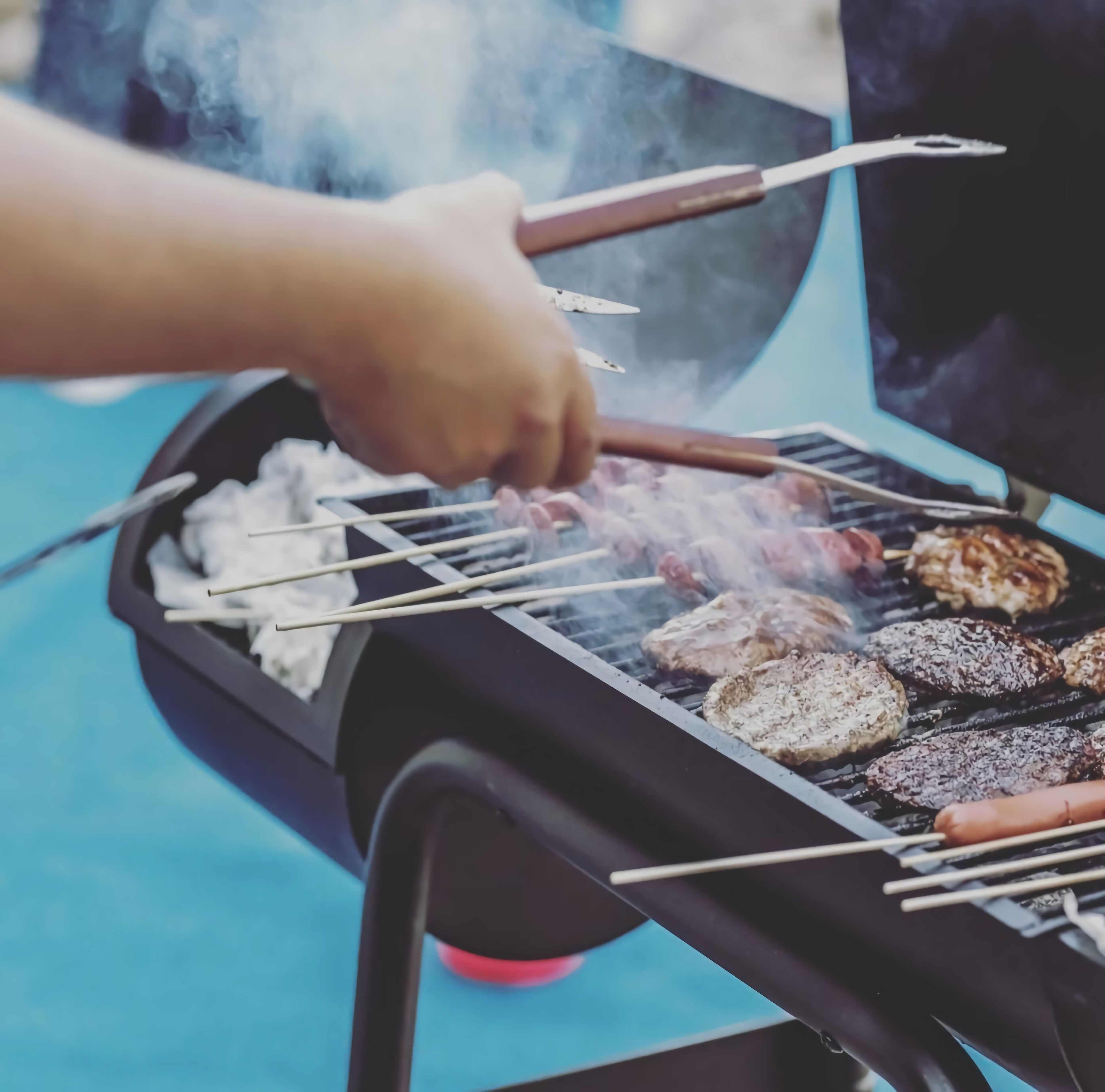 Une personne qui fait griller différents types de viande sur un barbecue à l’extérieur.