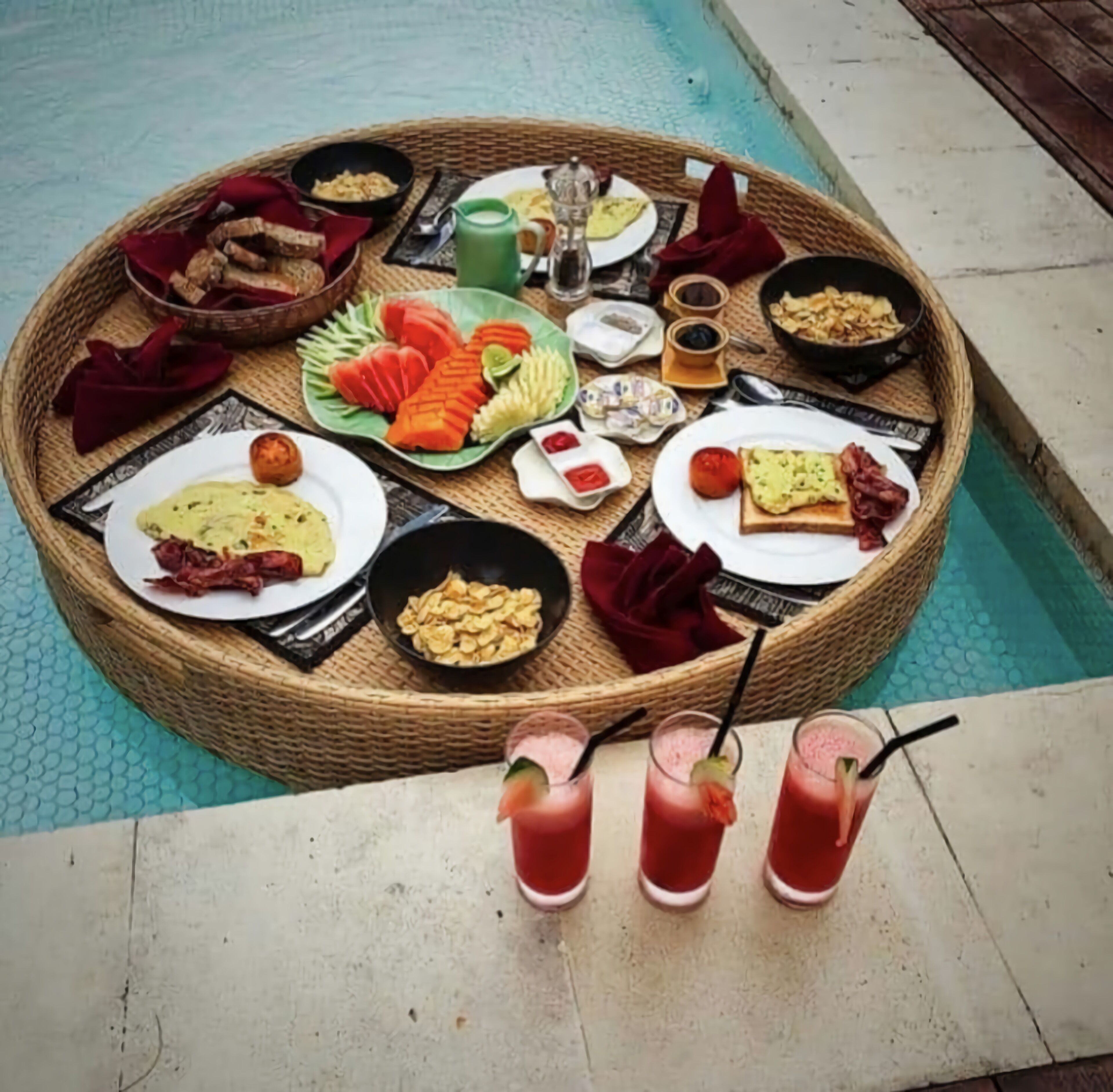 A round dining table with various dishes and drinks, surrounded by a pool.