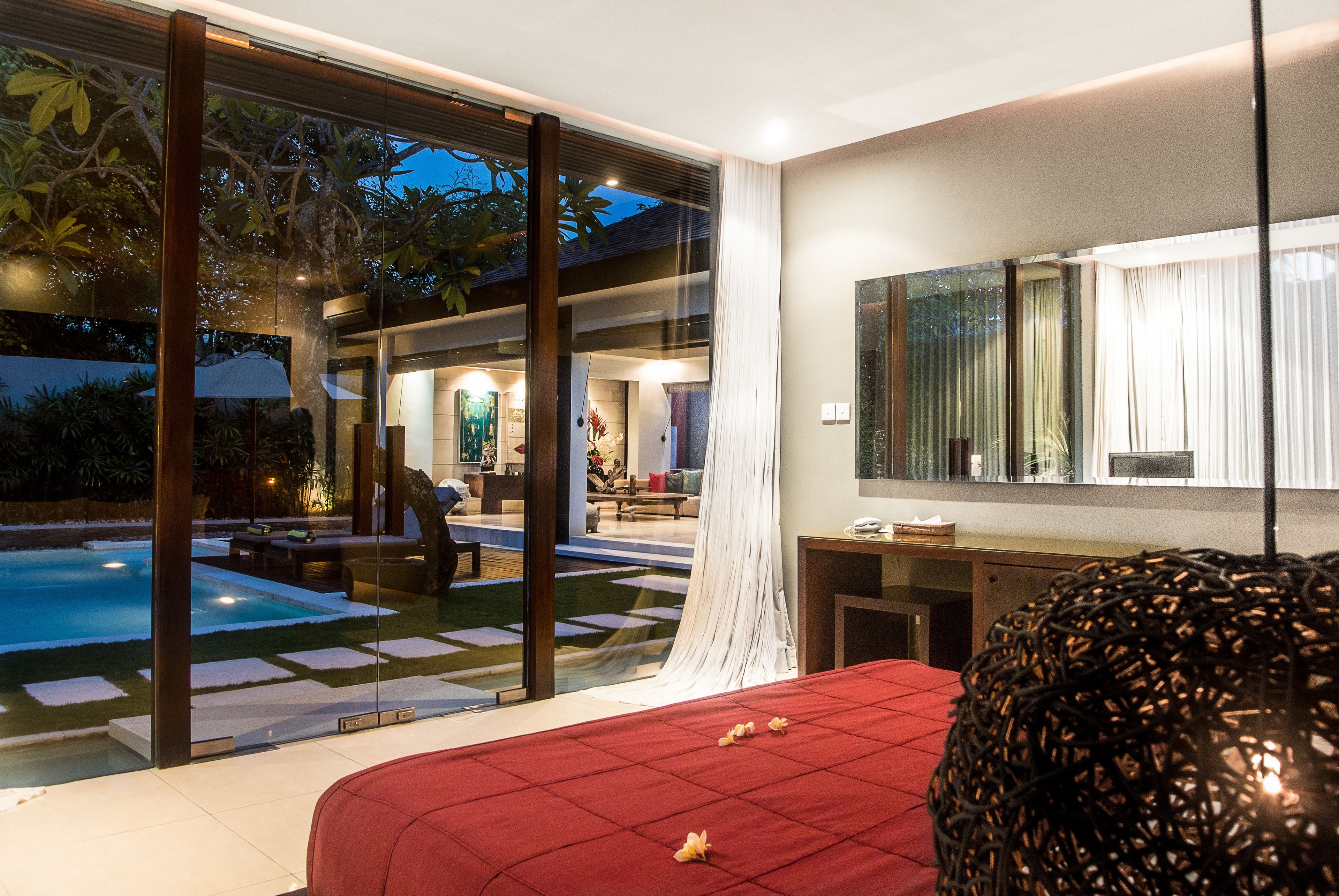 A modern hotel room with a large bed, a glass wall overlooking a swimming pool, and a view of the outdoor area.