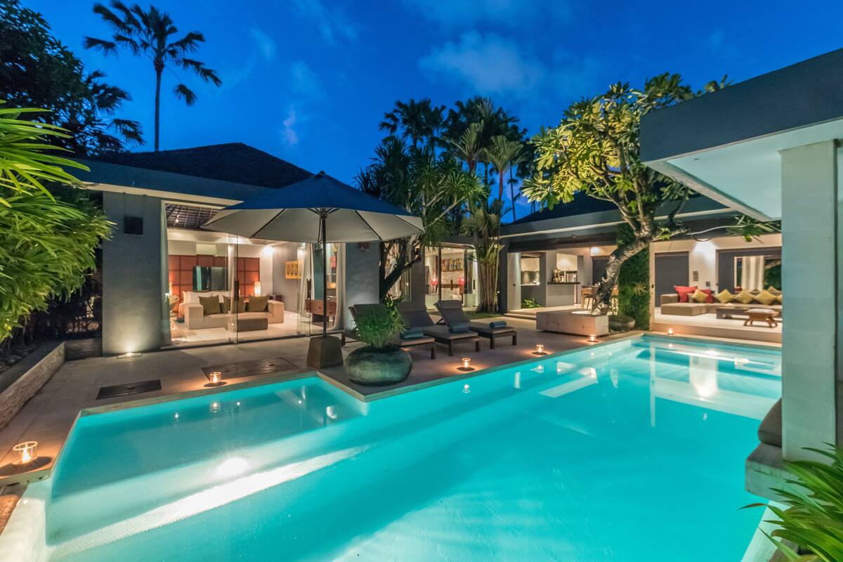 A modern pool area with a clear pool, lounge chairs, and a covered seating area.