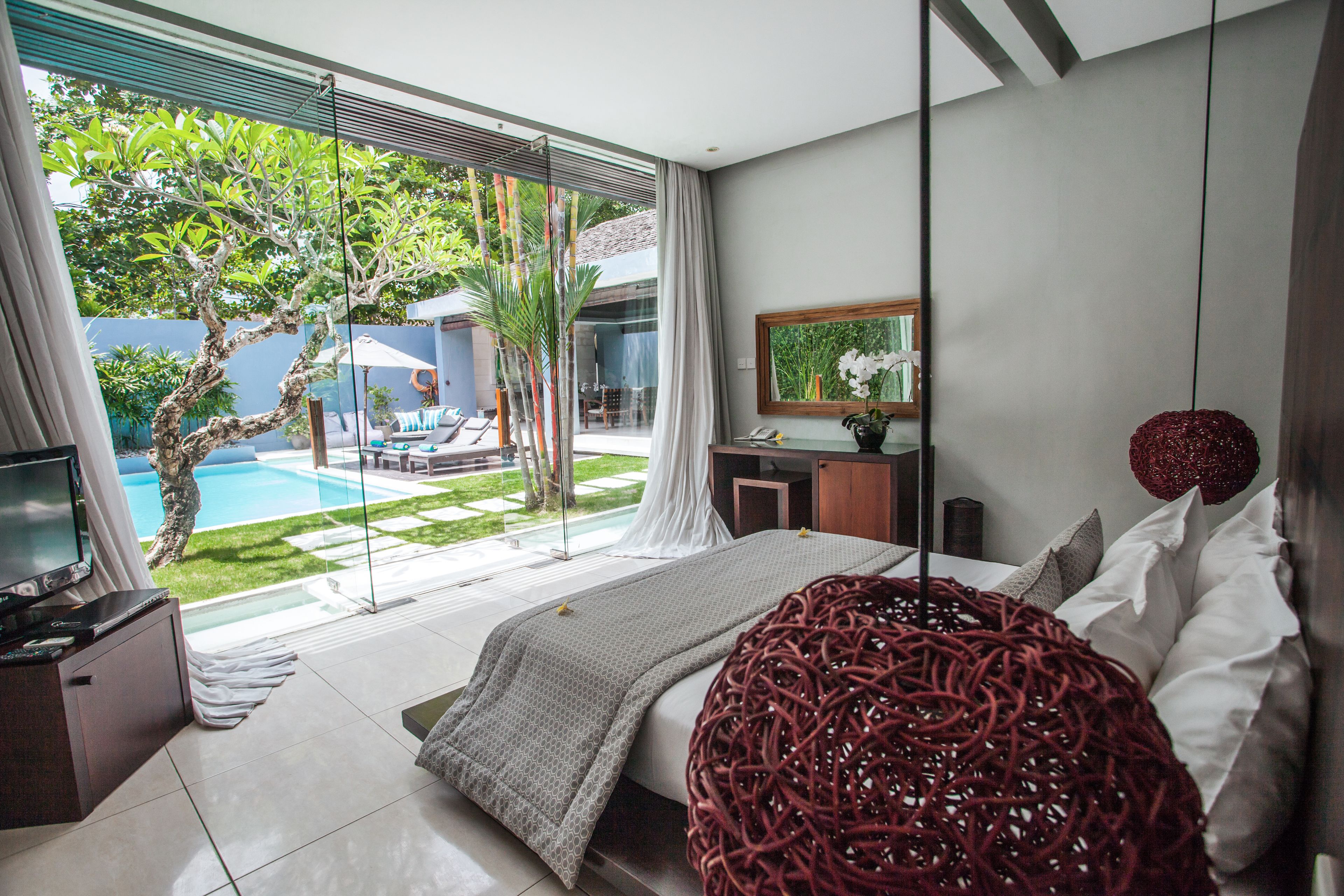 A modern bedroom with a large bed, a TV, and a view of a swimming pool and garden.