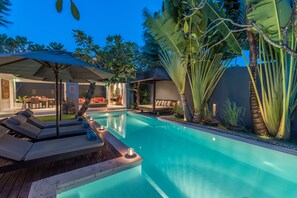 A swimming pool with lounge chairs and a covered seating area, surrounded by tropical plants. - Kembali Villas (Seminyak)