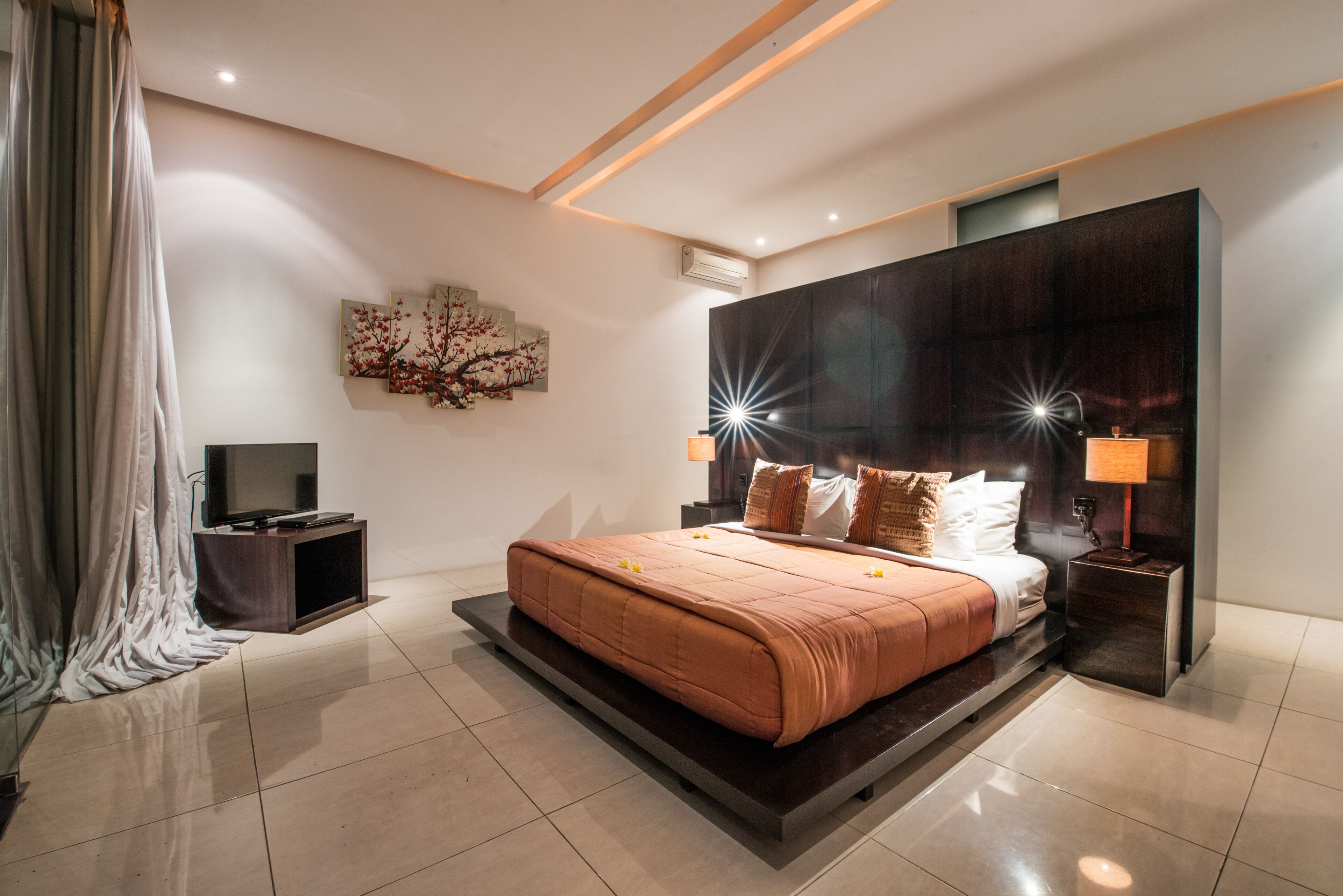 A modern bedroom with a large bed, a flat-screen TV, and a wall-mounted artwork.