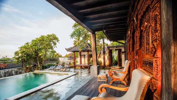 A pool area with wooden chairs and a covered section with intricate carvings. - The Kawan Jimbaran (Ungasan)