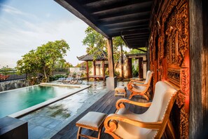 A pool area with wooden chairs and a covered section with intricate carvings. - The Kawan Jimbaran (Ungasan)