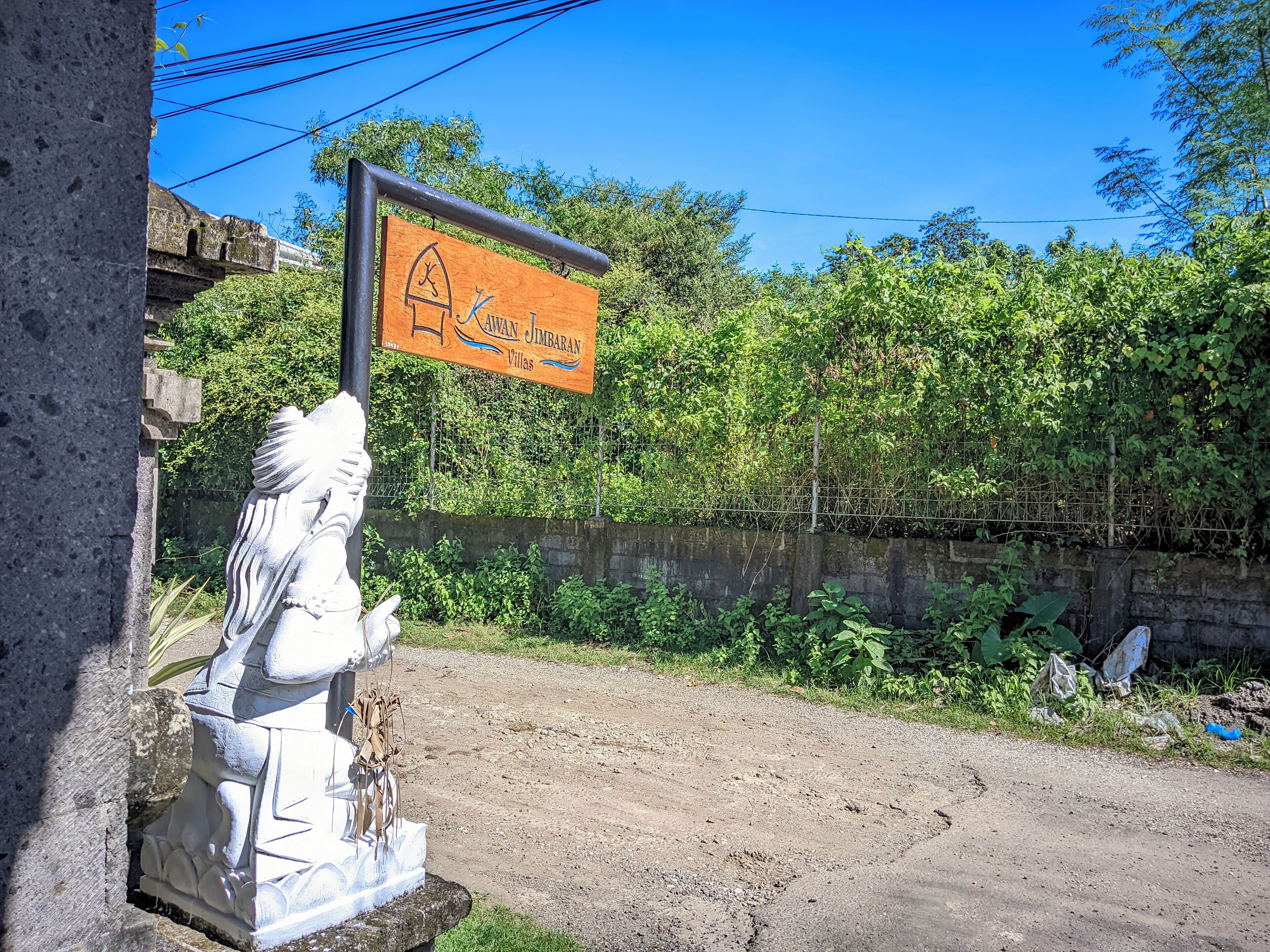 A sign for Kawan Jimbaran Villas with a statue of a figure in the foreground.