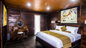 A wooden-paneled room with a large bed, a vanity with a mirror, and a painting on the wall. - The Kawan Jimbaran (Ungasan)