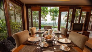 A dining area with a table set for four, surrounded by chairs, with a view of greenery and a distant landscape. - The Kawan Jimbaran (Ungasan)