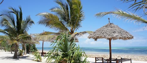 Aan een privƩstrand, wit zand, ligstoelen, parasols