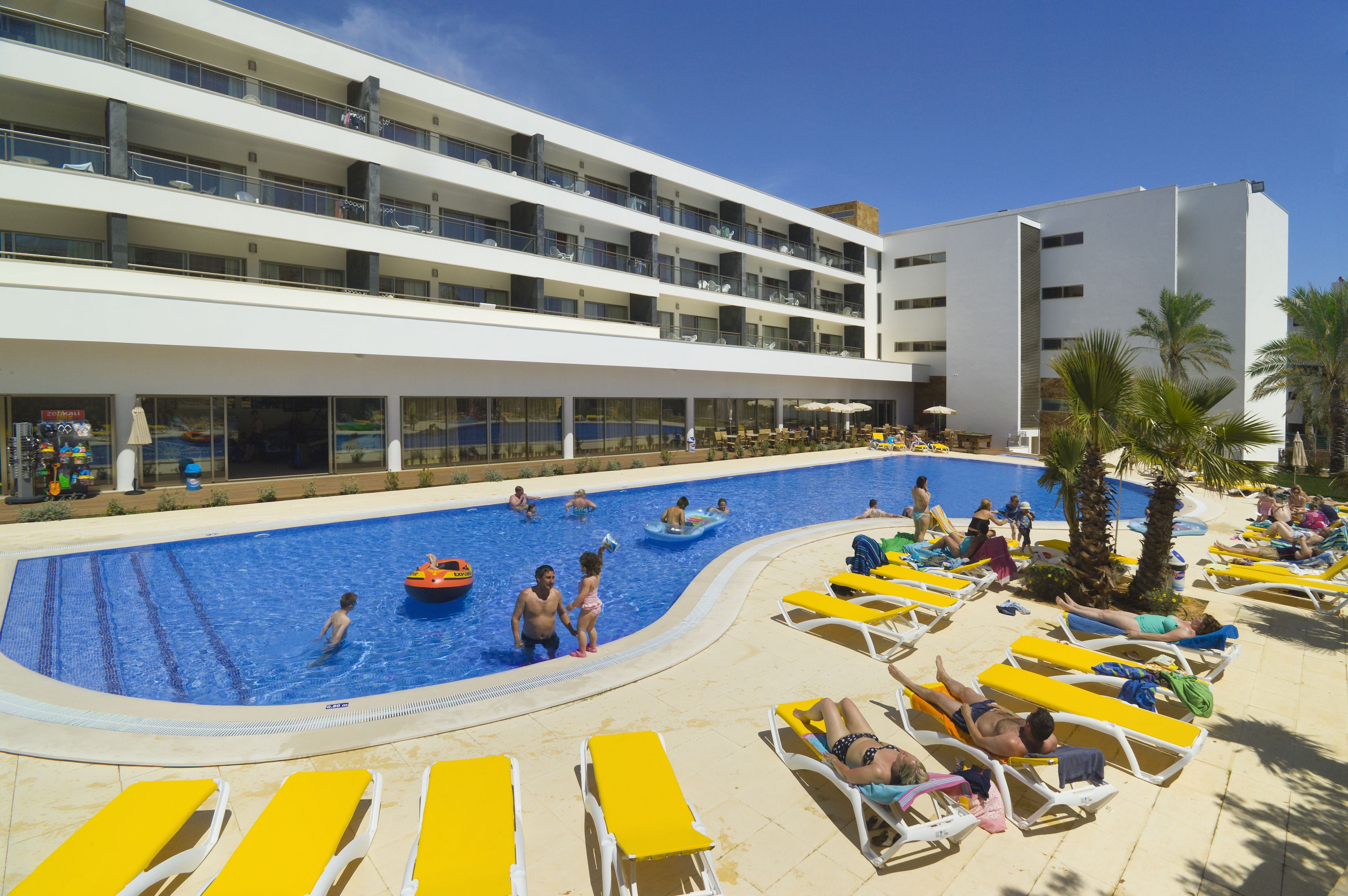 A pool area with multiple levels of balconies, sun loungers, and a clear blue sky.