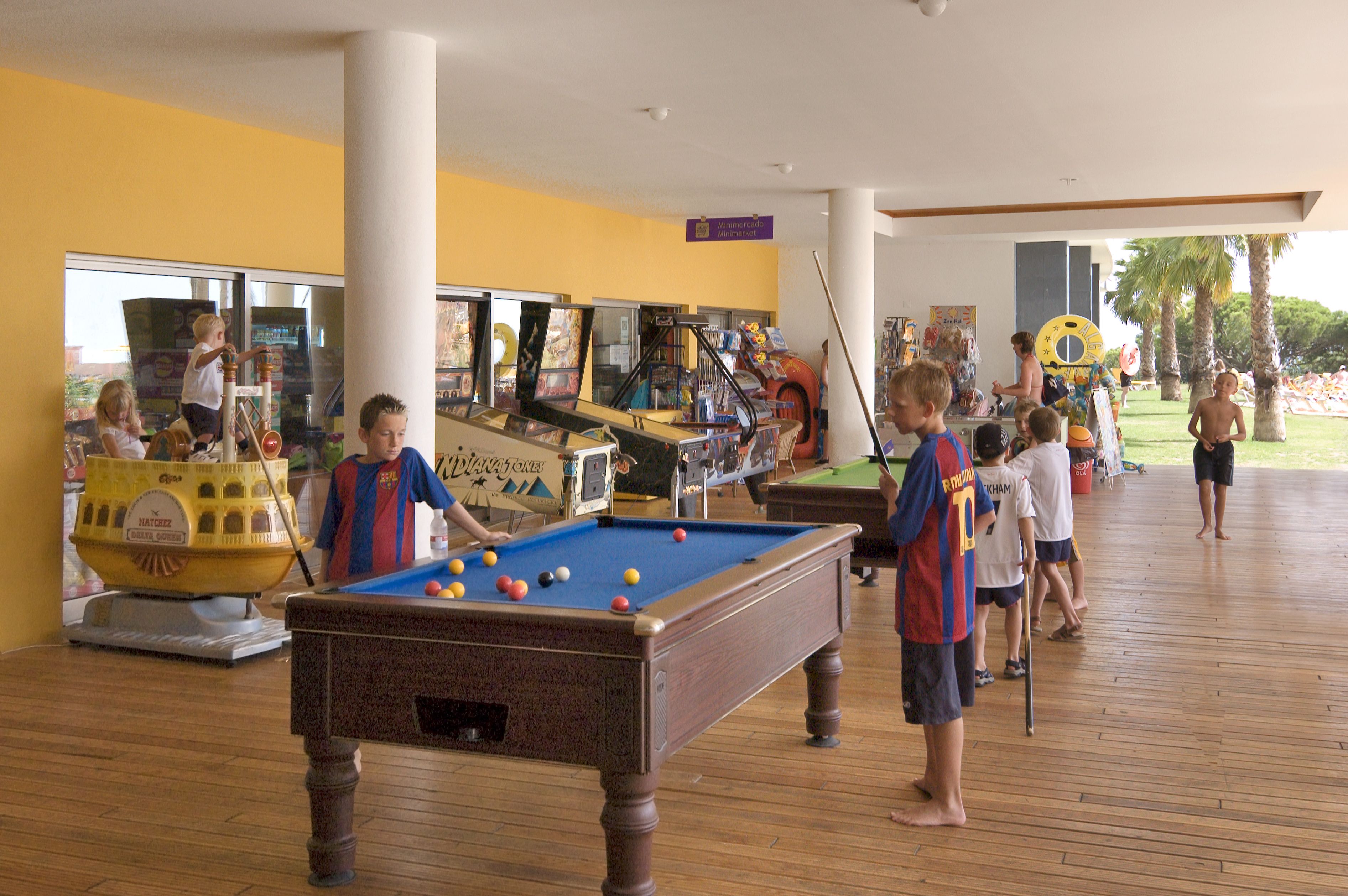 A pool table in a room with wooden flooring, surrounded by children playing.
