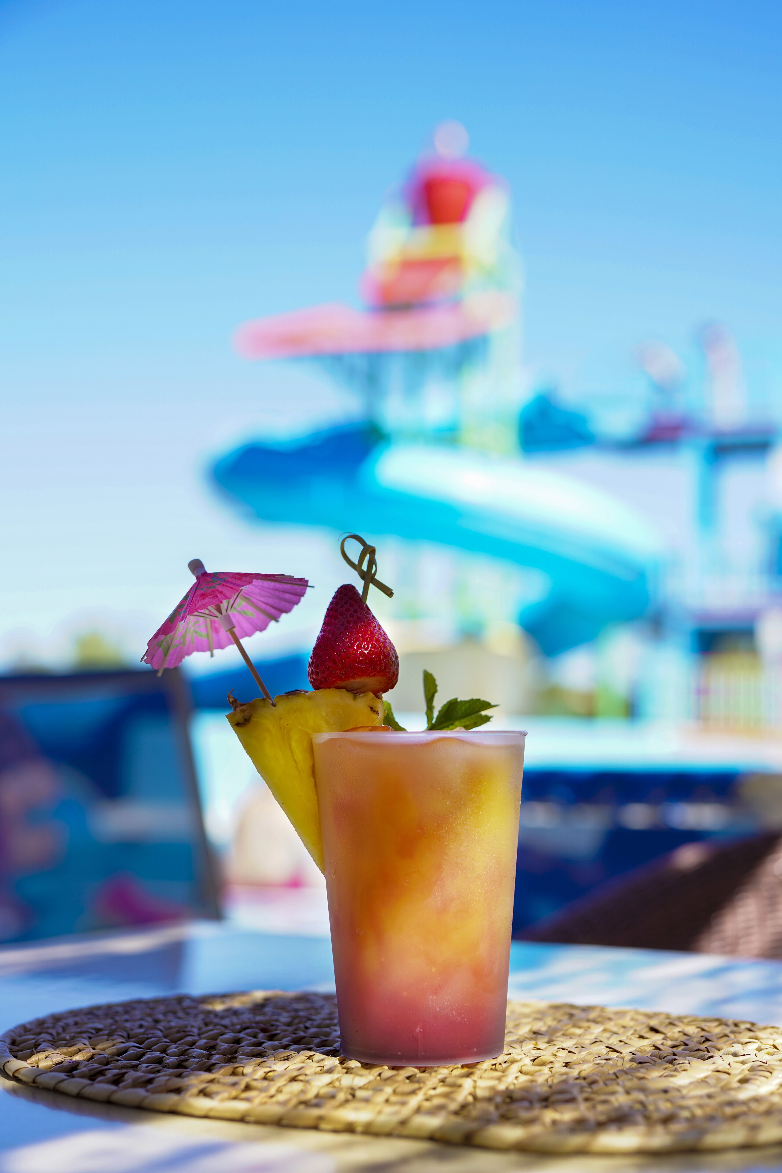 A tropical drink with a straw, a pineapple, and a strawberry on a woven placemat.