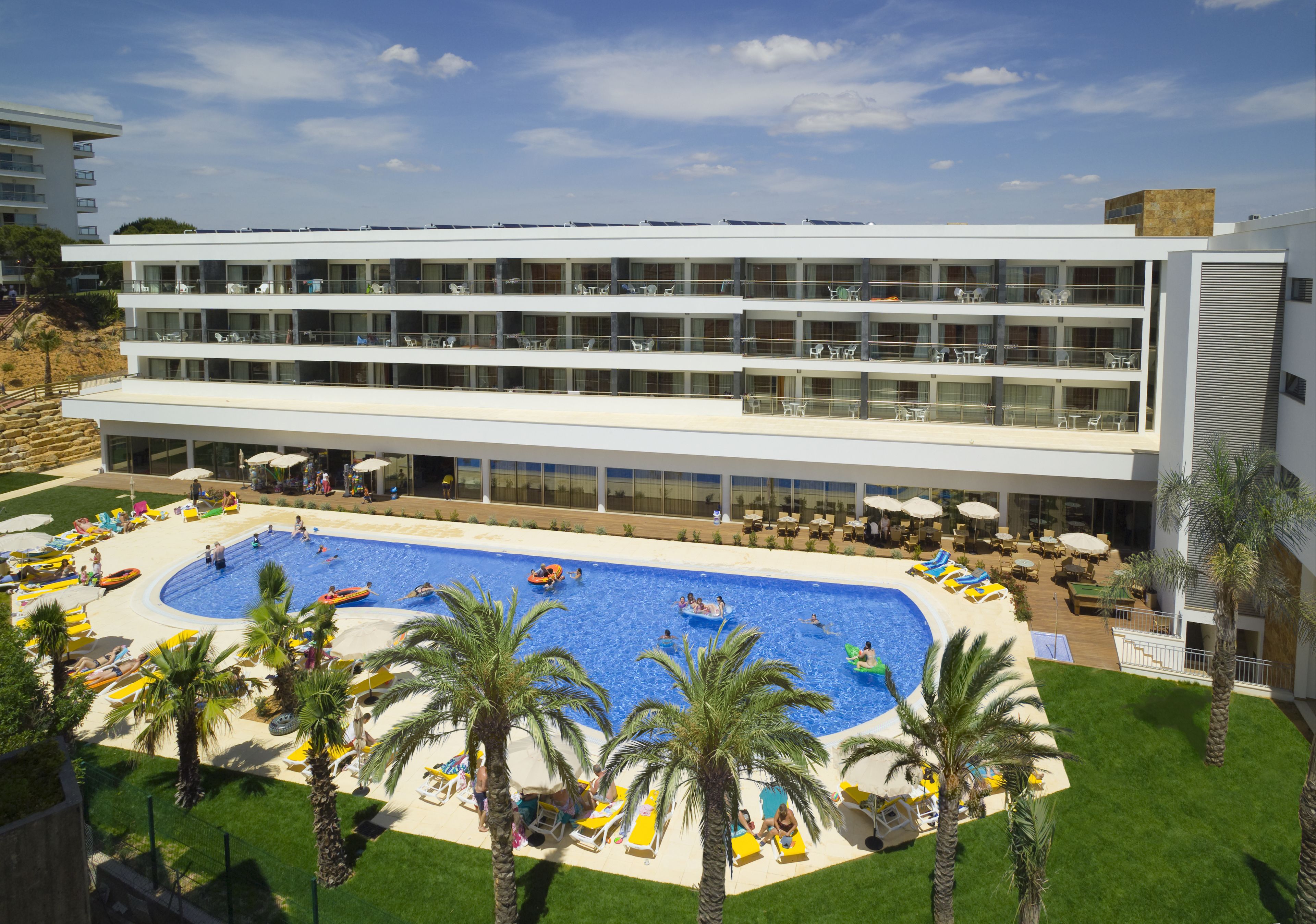 A modern hotel with a large pool, multiple balconies, and outdoor seating areas.