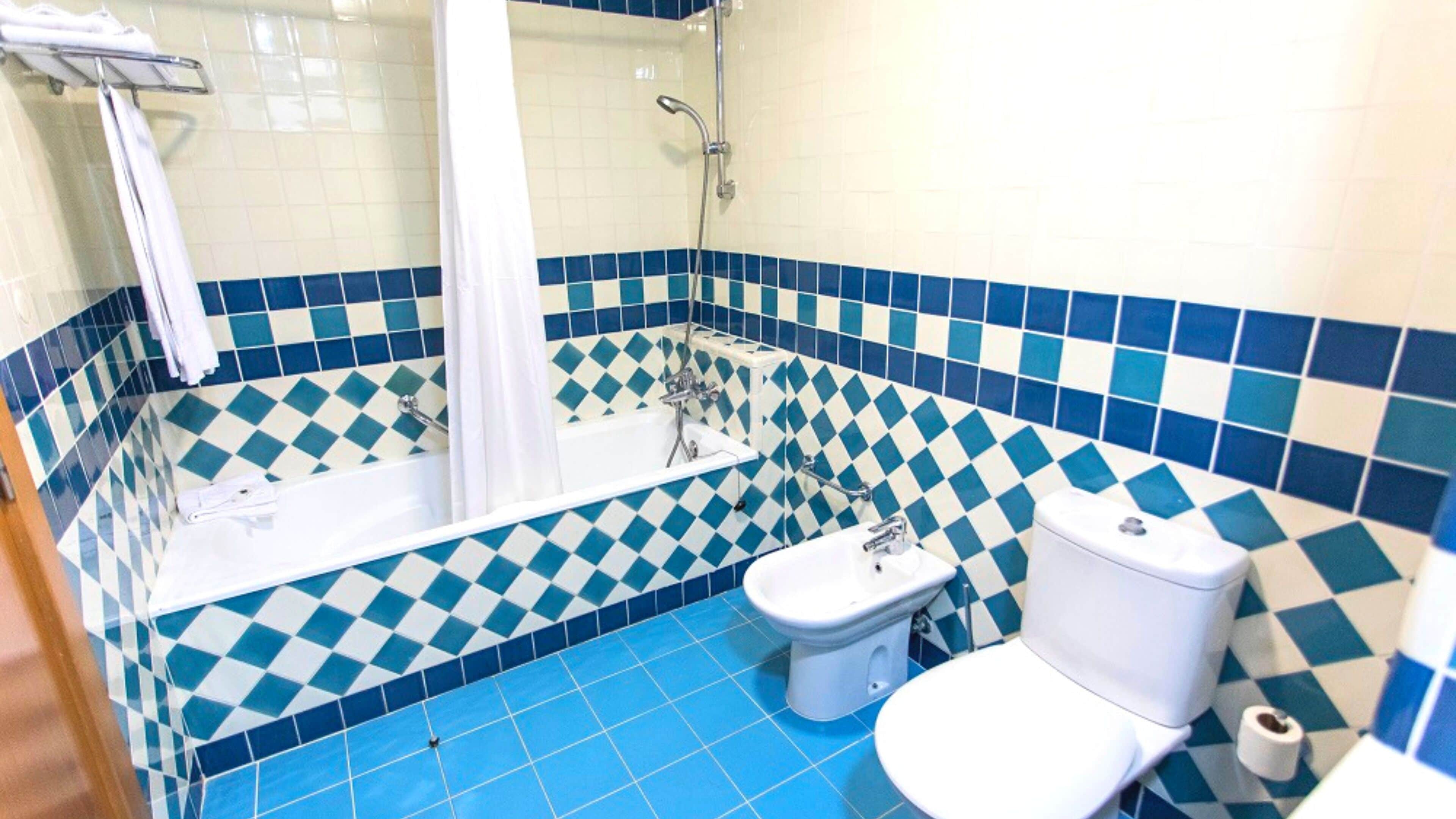 A bathroom with a blue and white checkered floor, a white bathtub, a white toilet, and a white sink.