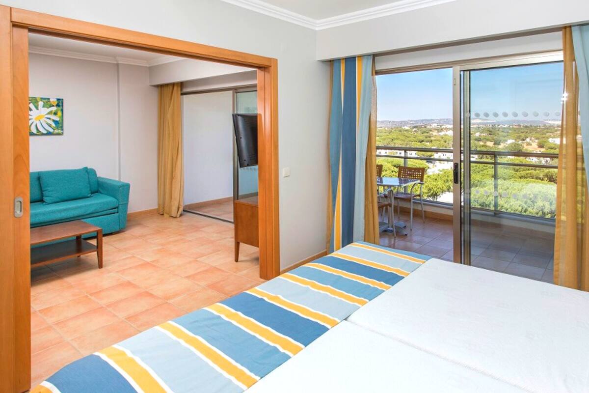 A hotel room with a bed, a sofa, a TV, and a balcony with a view.