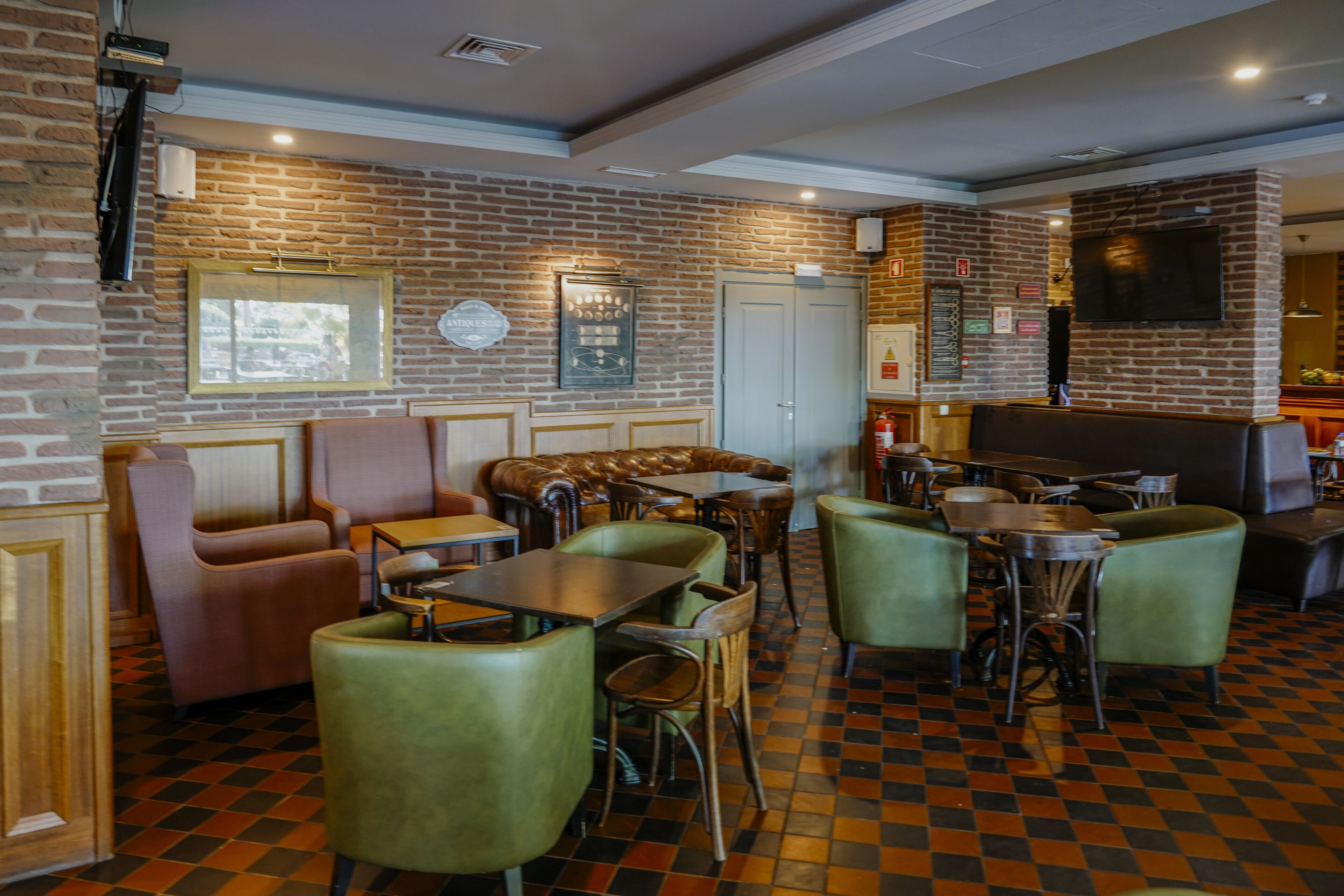 A restaurant interior with brick walls, checkered flooring, leather booths, and green chairs.