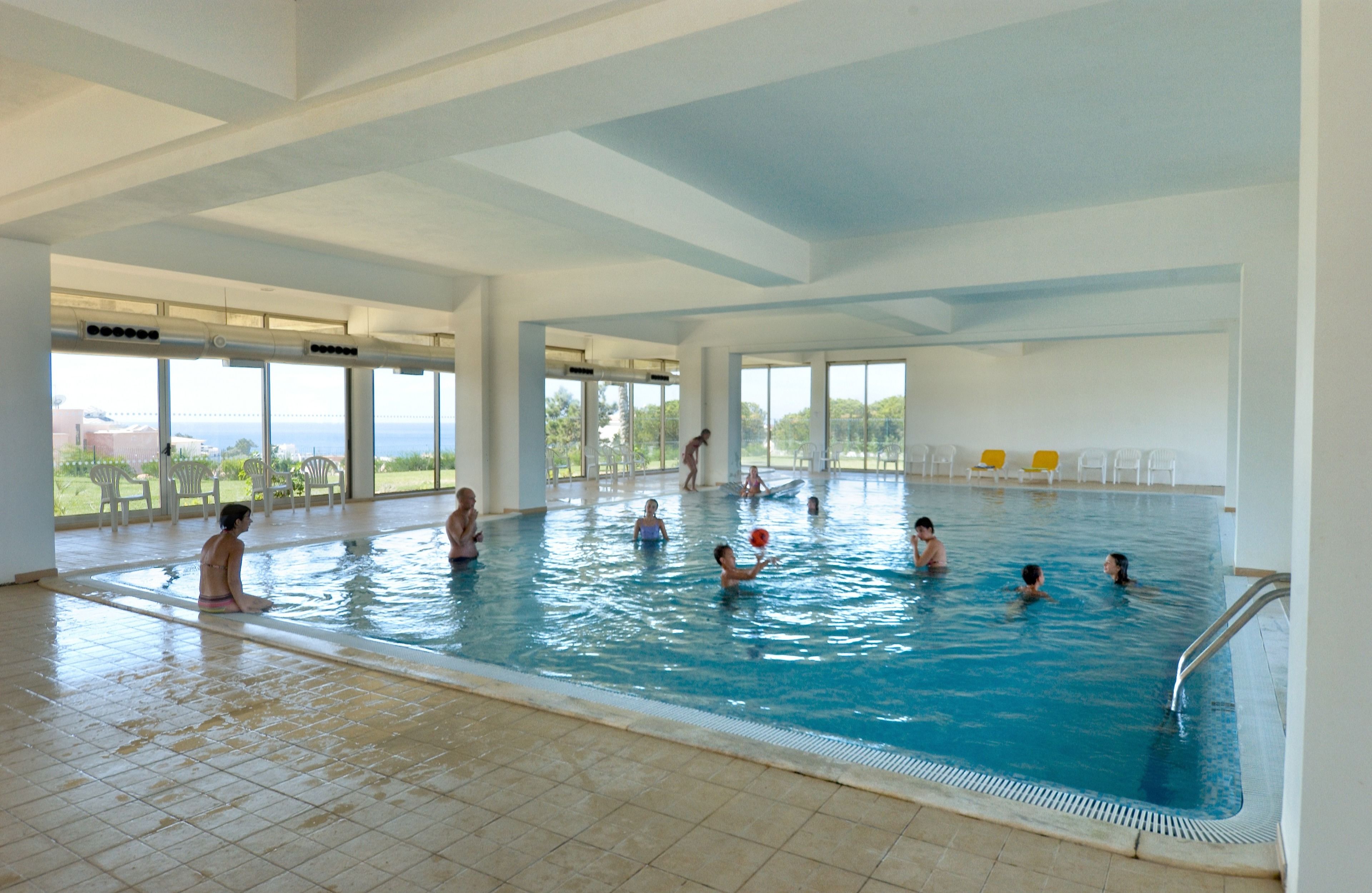 An indoor swimming pool with clear views of the outdoors, large windows, and a tiled floor.