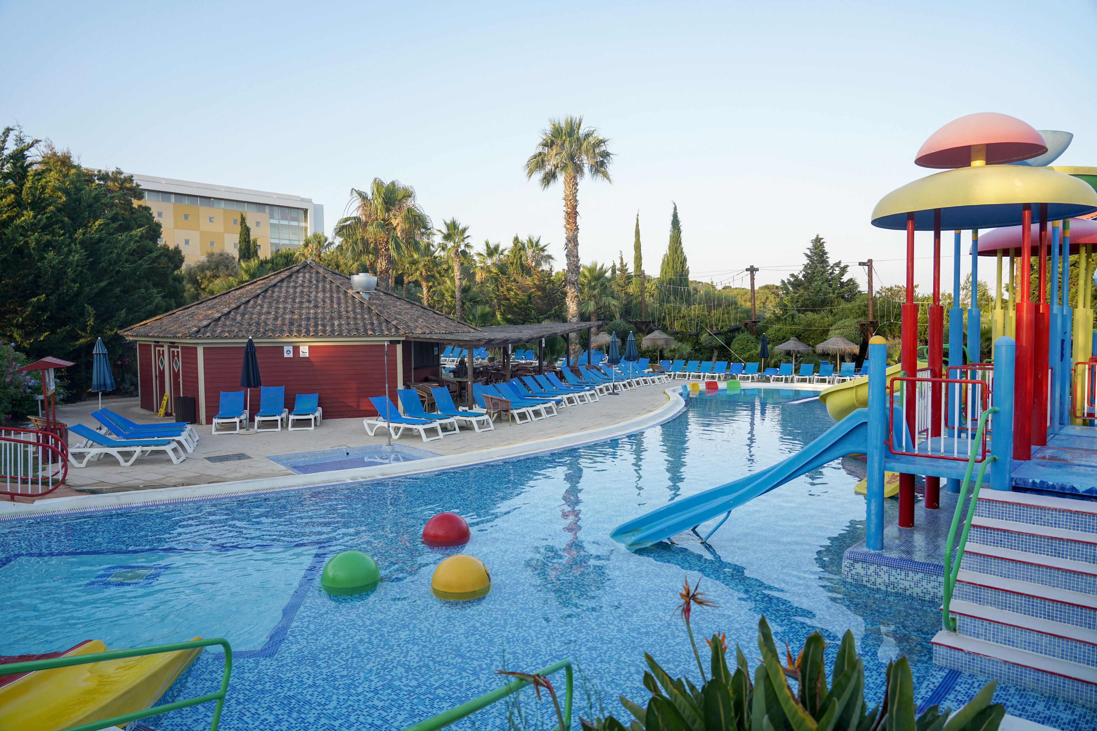 A swimming pool with a slide, lounge chairs, and a small pavilion.