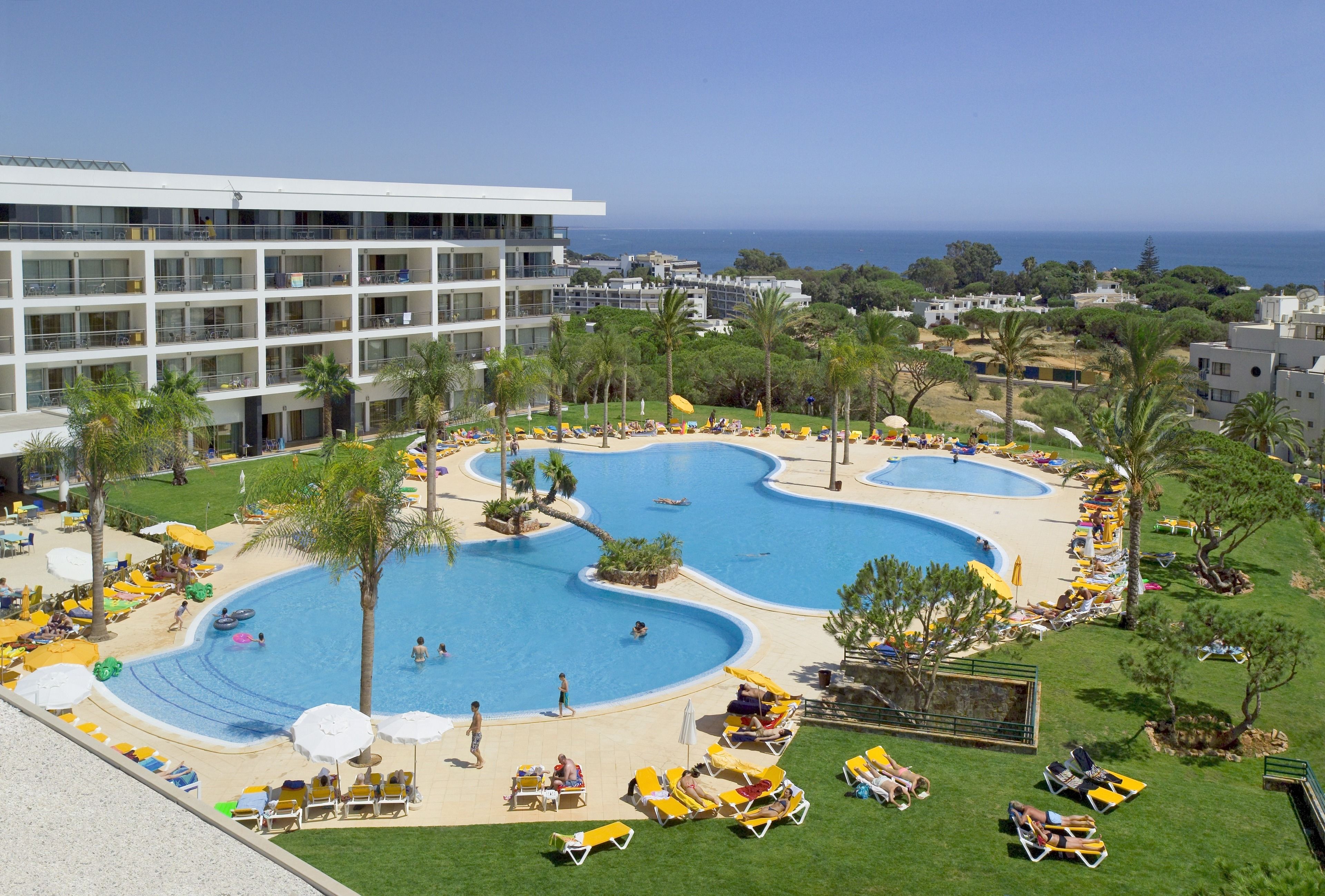 Un hôtel doté de plusieurs piscines, de chaises longues et offrant une vue sur la mer.