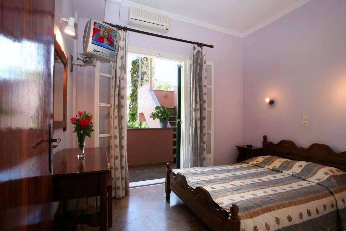 A bedroom with a bed, a desk, a chair, a TV, and a window with curtains.