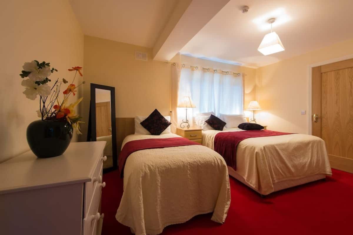 Ett hotellrum med två sängar, en byrå, en spegel och en vas med blommor.