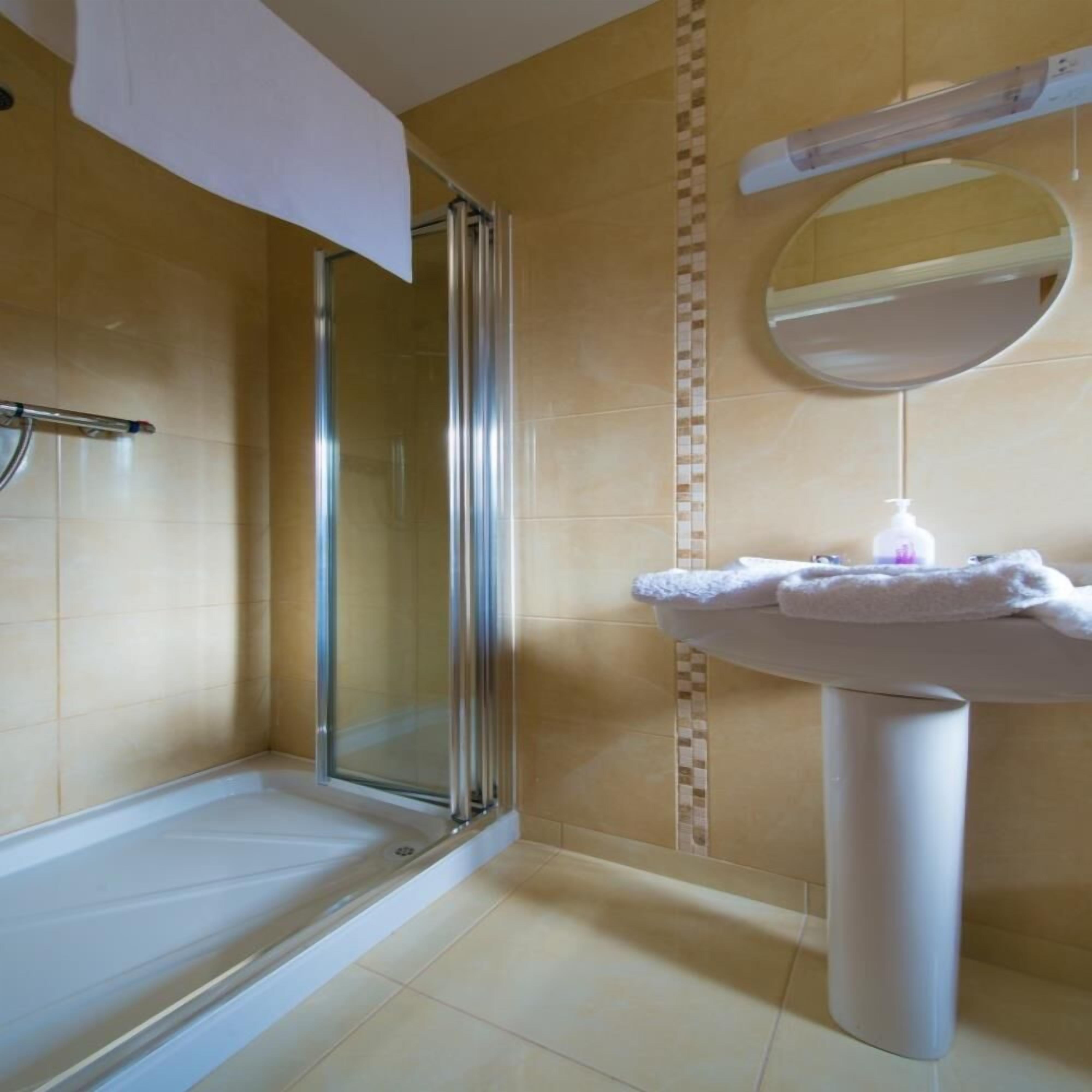 A bathroom with a glass shower enclosure, a white sink with a mirror above it, and a towel rack.