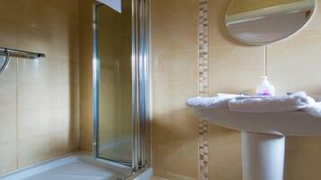 Un baño con cabina de ducha de vidrio, un lavamanos blanco con un espejo encima y un perchero para toallas.