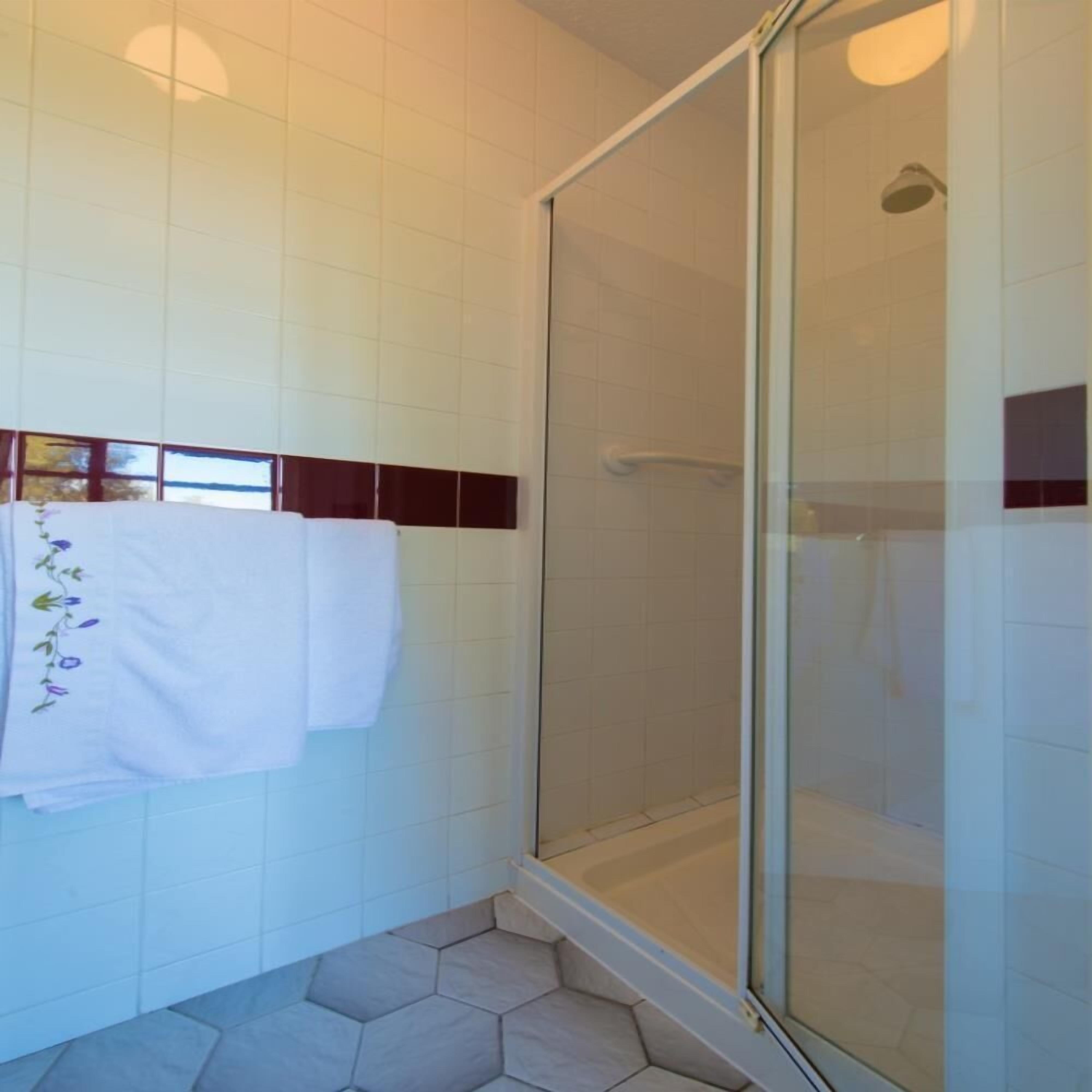 Un baño con paredes de azulejos blancos, cabina de ducha de vidrio y suelo de baldosas hexagonales.