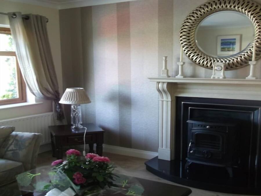 A living room with a fireplace, a mirror, a lamp, and a floral arrangement on a table.