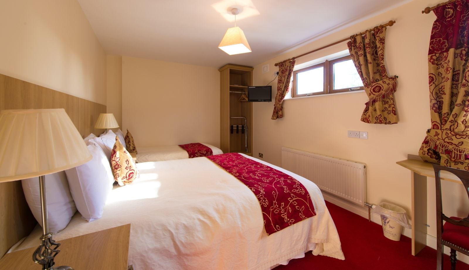 A hotel room with two beds, a desk, a chair, a TV, and a window with curtains.
