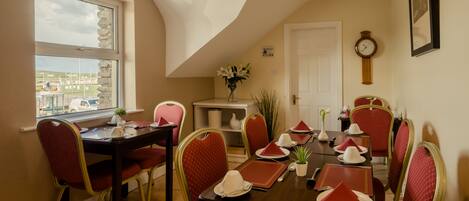 A dining area with a table set for six, red upholstered chairs, a vase with flowers, and a clock on the wall.
