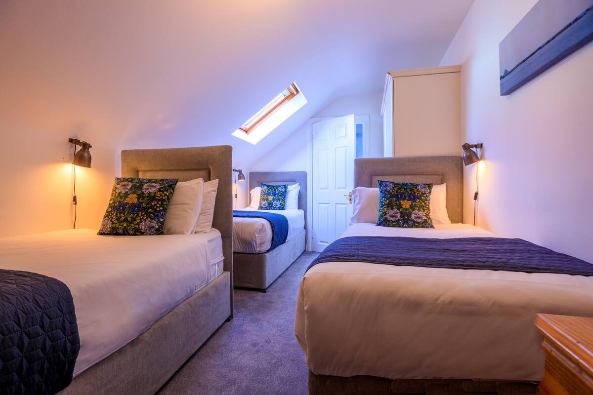 Habitación de hotel con dos camas, un tragaluz y una puerta que da a otra habitación.