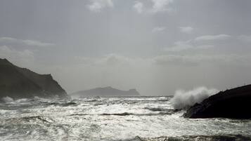 Paisaje costero con olas del mar agitadas chocando contra una costa rocosa.