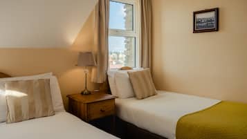 Una habitación de hotel con dos camas, una mesita de noche, una lámpara, una ventana con cortinas y un cuadro en la pared.