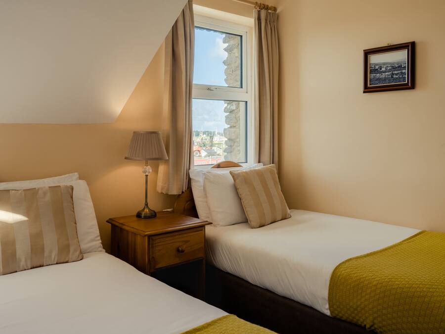 Una habitación de hotel con dos camas, una mesita de noche, una lámpara, una ventana con cortinas y un cuadro en la pared.